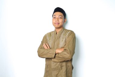 İslami elbise giyen barışçıl Asyalı Müslüman adam kollarını kavuşturup izole beyaz arka planda duran kameraya bakıyor.