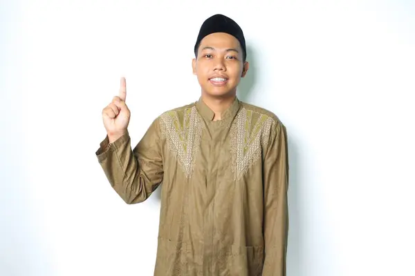 stock image smiling asian muslim man pointing to above wearing islamic dress isolated on white background