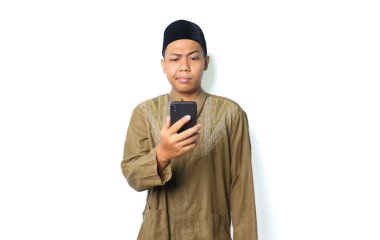 Kafası karışmış Asyalı Müslüman adam beyaz arkaplanda izole edilmiş akıllı telefon programı düşünce ifadesi kullanarak mesajı okuyor.