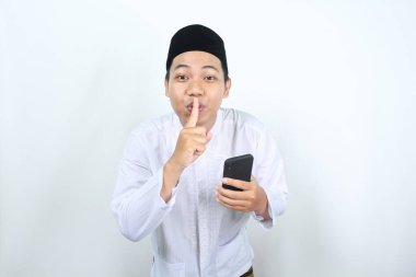 Gülümseyen Asyalı Müslüman adam telefonu tutarken sessiz bir jest yapıyor.