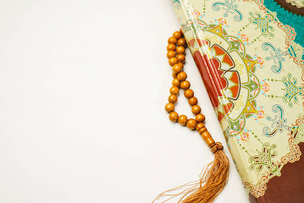 The Holy Al Quran with written arabic calligraphy meaning of Al Quran and rosary beads or tasbih on white background with copy space.