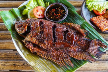 Kızarmış guram ya da ızgara guram, kırmızı barbekü sosu, sebze ve kırmızı biber sosu muz yaprakları üzerinde servis edilir.