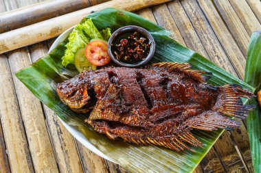 Kızarmış guram ya da ızgara guram, kırmızı barbekü sosu, sebze ve kırmızı biber sosu muz yaprakları üzerinde servis edilir.