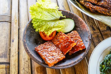 Kızarmış tempeh ya da kırmızı barbekü soslu kızarmış tempeh, sebze ve biber sosu bir toprak havanında servis edilir.