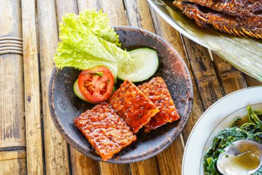 Kızarmış tempeh ya da kırmızı barbekü soslu kızarmış tempeh, sebze ve biber sosu bir toprak havanında servis edilir.