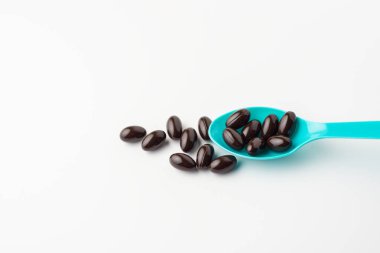 Beyaz arka planda mavi kaşıkta siyah yumuşak kapsüller. Vitamin takviyesi