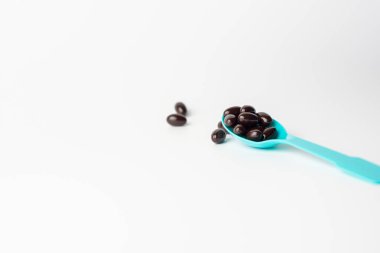 Beyaz arka planda mavi kaşıkta siyah yumuşak kapsüller. Vitamin takviyesi