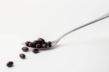 Beyaz arka planda paslanmaz çelik bir kaşıkta siyah yumuşak jel kapsüller. Vitamin takviyesi