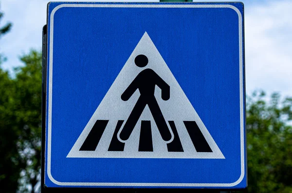 Ön planda bir yaya geçidinin varlığını gösteren renkli yol işareti var.