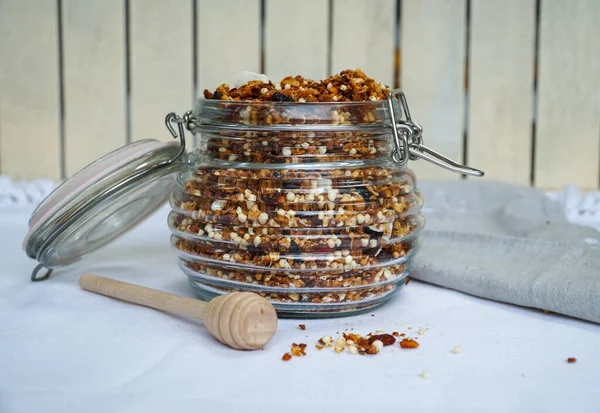 stock image A homemade granola-filled jar on a wooden white background, presenting a delectable mix of oats, nuts, seeds, and honey a wholesome and visually appealing treat.