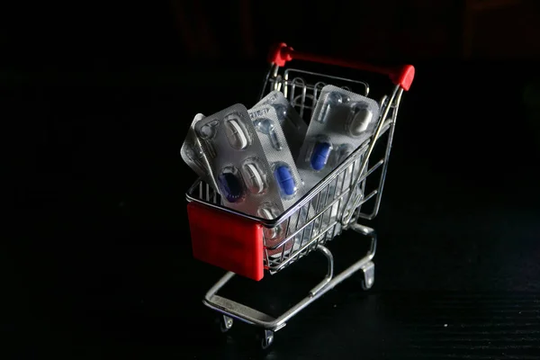 View of a mini supermarket cart with pills in a black background