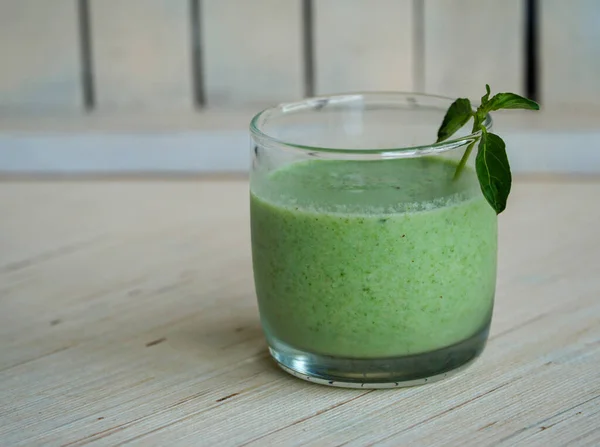 Front view of a glass of green smoothie with mint in a white background