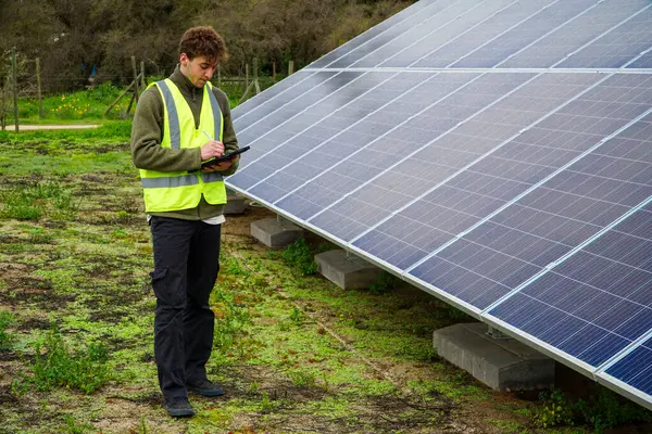 A young industrial engineer in uniform walking through the solar panel field for monitoring.