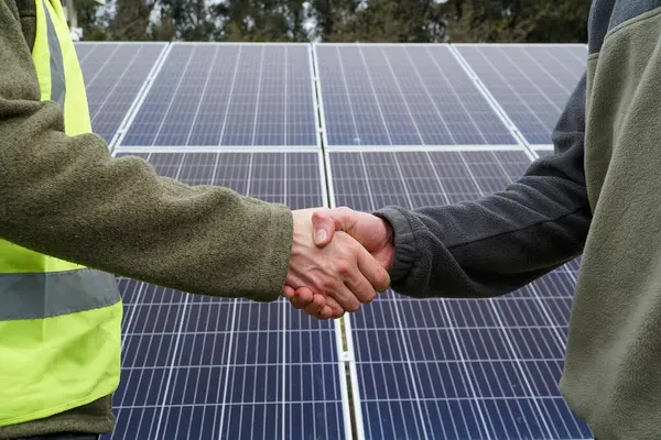Two people shaking hands, sealing a deal in front of solar panels. Concept of business, sustainability, agreements, innovation, and science.