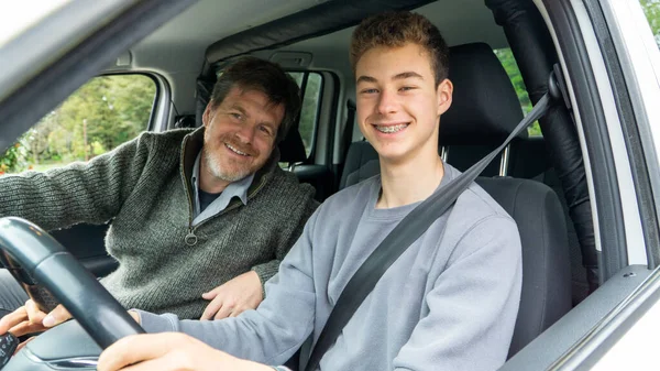 Teenager and father in the car, smiling at the camera.