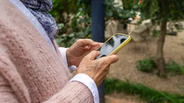 Close-up view of elderly hands typing on a mobile phone in the garden.