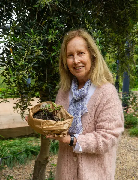 Portrait of a joyful and content elderly woman, happily holding a plant, ready to place it in her garden.