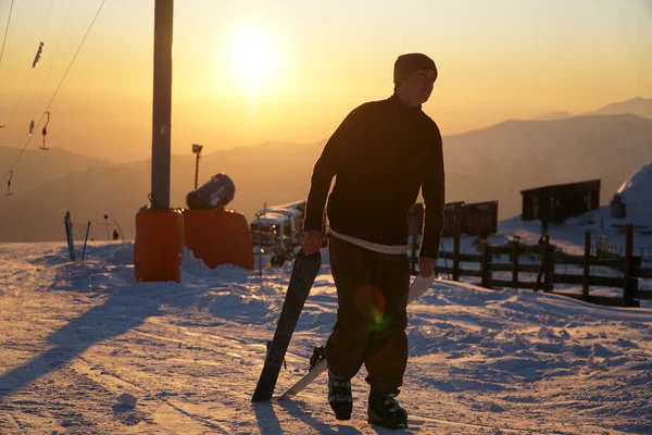 Young person carrying skis in the mountains during the sunset.
