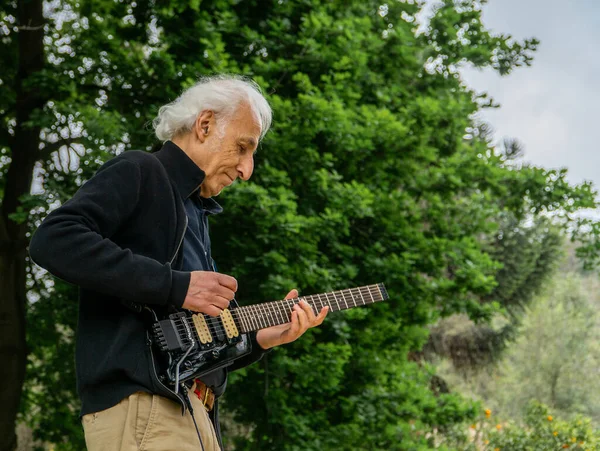 Elderly man jamming on an electric guitar with friends outdoors.
