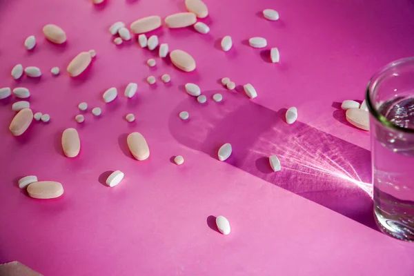 Pink background with scattered pills and the shadow of a glass of water.
