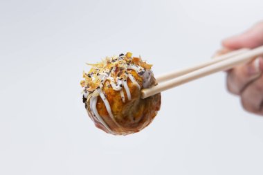 Takoyaki (Octopus Balls) yemek çubuklarıyla toplanır, izole edilmiş beyaz arka planda detaylı çekim yapılır