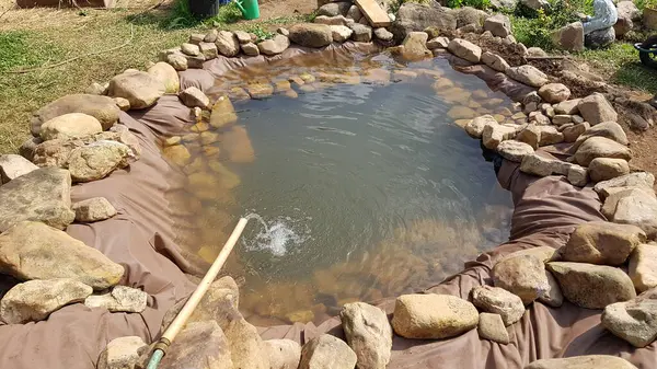 water jet falling on homemade pond in the garden. make pond at home step by step with rocks and cloth