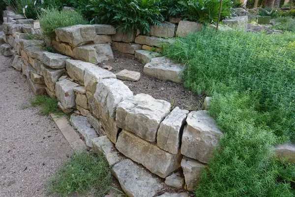 A stone wall with a small garden in front of it. The garden has some plants and a few rocks