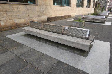Çağdaş taş kiremitler ve saksılarla çevrili açık bir şehir meydanında metal sırtı olan beton banklar..