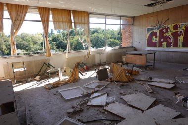Kırık mobilyaların, yırtık perdelerin, kırık camların ve duvarlarda graffitilerin olduğu terk edilmiş bir sınıf.
