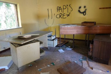 A vandalized office in an abandoned school, featuring broken desks, scattered debris, and graffiti on the walls. clipart