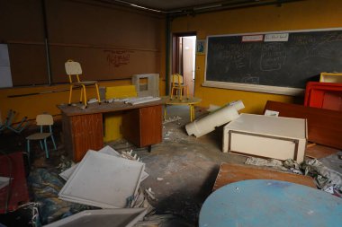 Dağınık mobilyaları, dağınık döküntüleri ve grafiti kaplı karatahtayla dolu ihmal ve çürümeyi yansıtan dağınık bir sınıf..
