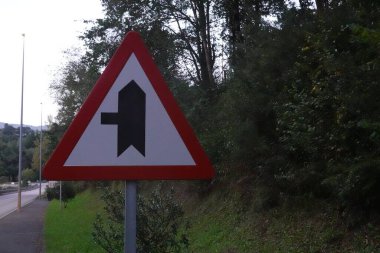 Alacakaranlıkta ormanın kenarındaki yol kenarında bir kavşağın yaklaştığını gösteren üçgen bir işaret..