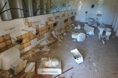 Bozuk lavaboları, tuvaletleri ve döküntüleri döşenmiş döşemeleri olan terk edilmiş bir okulda tahrip edilmiş bir banyo..