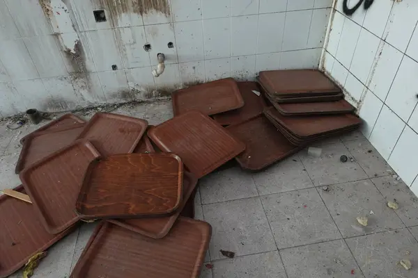 stock image A pile of brown trays sits in a corner of an abandoned school kitchen, surrounded by dirt and signs of decay.