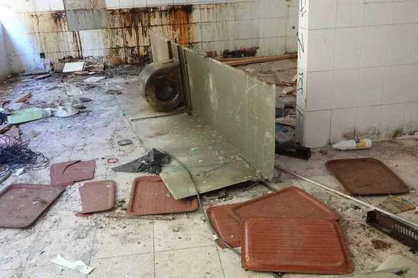 Stock image A derelict school kitchen filled with broken equipment, dirty trays, and rusted surfaces, showing signs of neglect and decay.