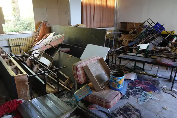 stock image A disorganized, abandoned school room filled with broken furniture, debris, and scattered objects, showing signs of neglect and decay.