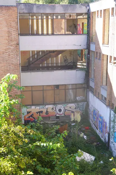 Stock image An overgrown courtyard of an abandoned school building, featuring graffiti on walls and broken windows.