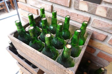 Kırsal ahşap bir sandıkta dizilmiş yeşil elma şarabı şişeleri ve her şişenin mantarları. Tozlu şişeler eski depolarını yansıtıyor, tuğla bir duvara yaslanmış, geleneksel bir şekilde..