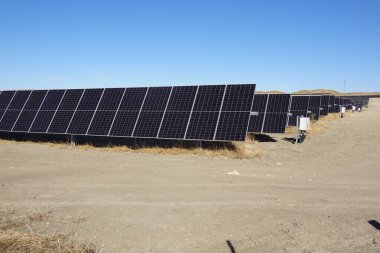 Açık mavi gökyüzünün altında kuru ve çorak bir arazide geçen büyük bir güneş çiftliğinin güneş panellerine yakın çekim..