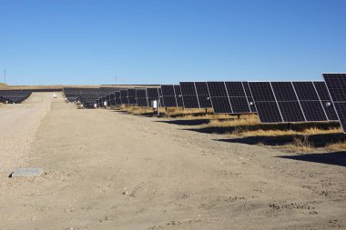 Geniş bir güneş çiftliğindeki güneş panelleri kuru bir arazide toprak bir yol ile berrak bir gökyüzünün altında..