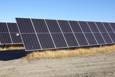 Close-up view of solar panels installed on a dry, barren landscape under a clear blue sky. clipart