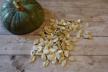 Arkaplanda yeşil bir balkabağı ile ahşap yüzeye yayılmış balkabağı tohumları hasat edildi.