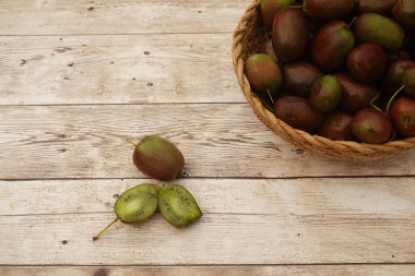Olgun sert kiviler (aktinidia arguta), bir hasır sepetin içinde ve kırsal ahşap bir masanın üzerinde canlı yeşil iç kısımlarını göstererek sunulurlar.