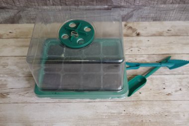 Mini greenhouse propagator kit with small shovel and gardening tools sitting on a wooden table, ready for seed starting clipart