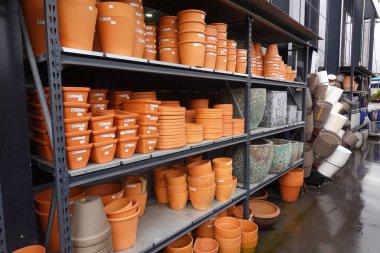 Terracotta ve plastik saksıların çeşitli boyutları ve renkleri bir bahçe merkezindeki metal raflarda düzgünce istiflenmiştir, satılmaya hazırdır.