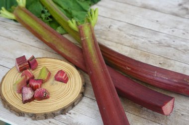Canlı kırmızı rhubarb sapları ahşap bir masanın üzerinde, yeni doğranmış parçaları sergilenen ahşap bir diskin yanında, aşçılık kullanımına hazır.