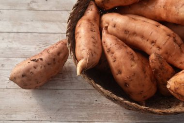 Tahta bir masanın üzerindeki dokuma sepetin içinde taze çiftlik ürünlerinin özünü somutlaştıran birkaç tatlı patates yatıyor.