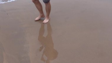 Çıplak ayaklı gezgin, nemli kıyı şeridi boyunca yürüyor, el değmemiş kıyı manzarasını sakin yaz tatilinde geçerken geçici ayak izleri yaratıyor.