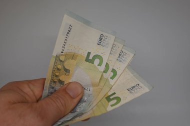 El ele tutuşan üç beş avroluk banknot, temiz, sade beyaz bir arkaplan, para birimi ve finans konularını ön plana çıkarıyor