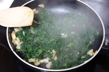 Isırgan otları ve soğanlar tavada pişiyor, buharı serbest bırakıyor, ahşap bir spatulayla karıştırılıyor, ısırgan otlu yumurta tarifinin bir parçası.